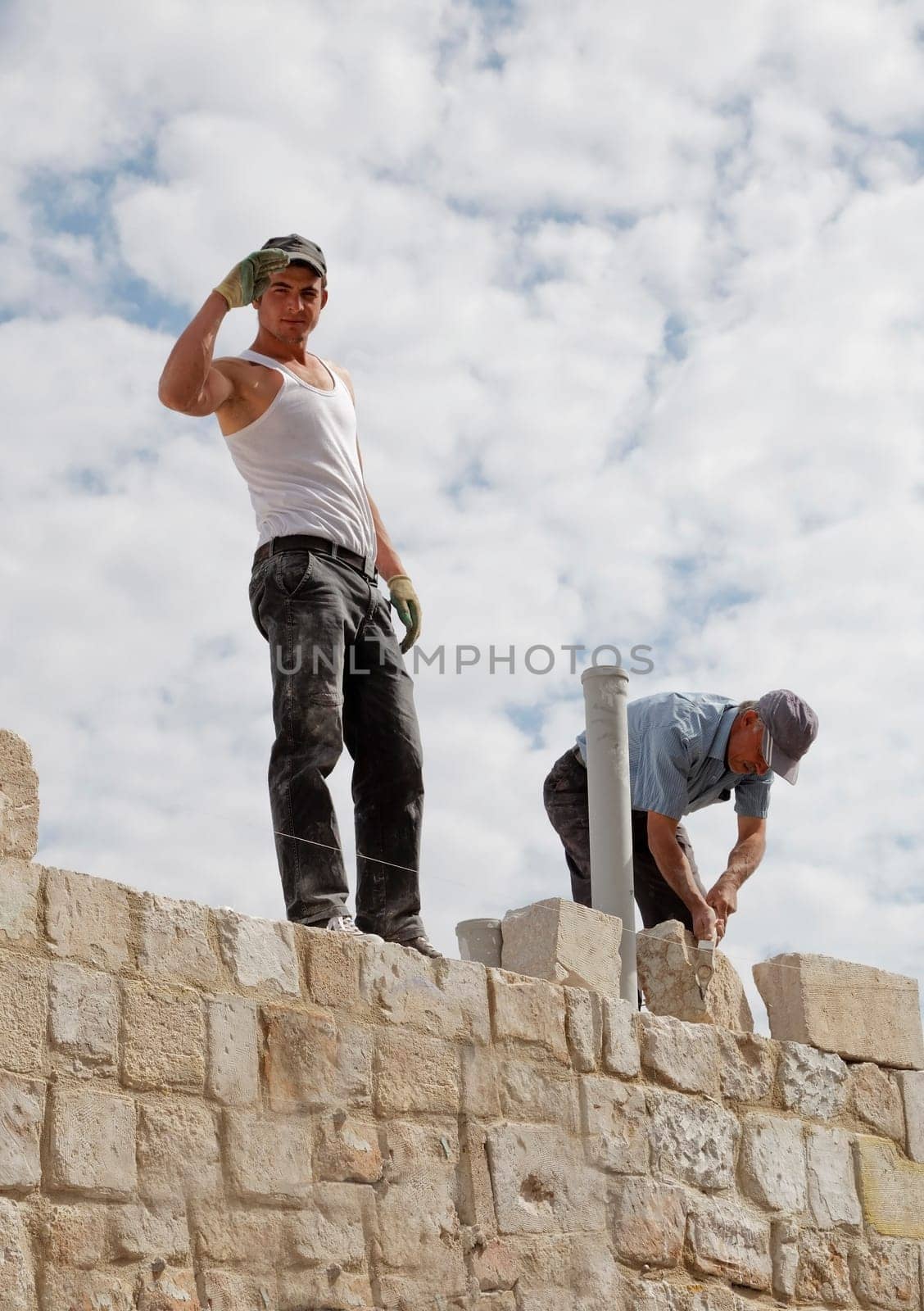 Goreme, Cappadocia, Turkey - June, 2011: Men at work, handsome body toned Turkish builder saluting under a bright cloudy sky from an elevated position. Brickie laying bricks.