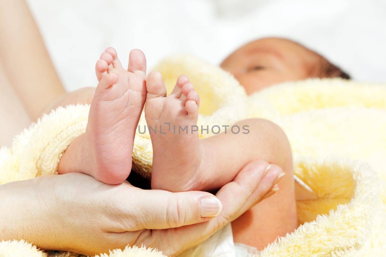 Newborn baby feet in mother&#039 s hands with soft yellow blanket