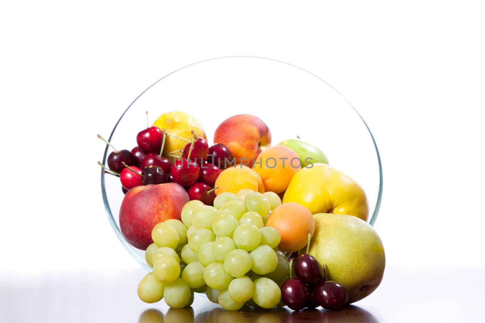 Glass bowl of fruit on a table against white background