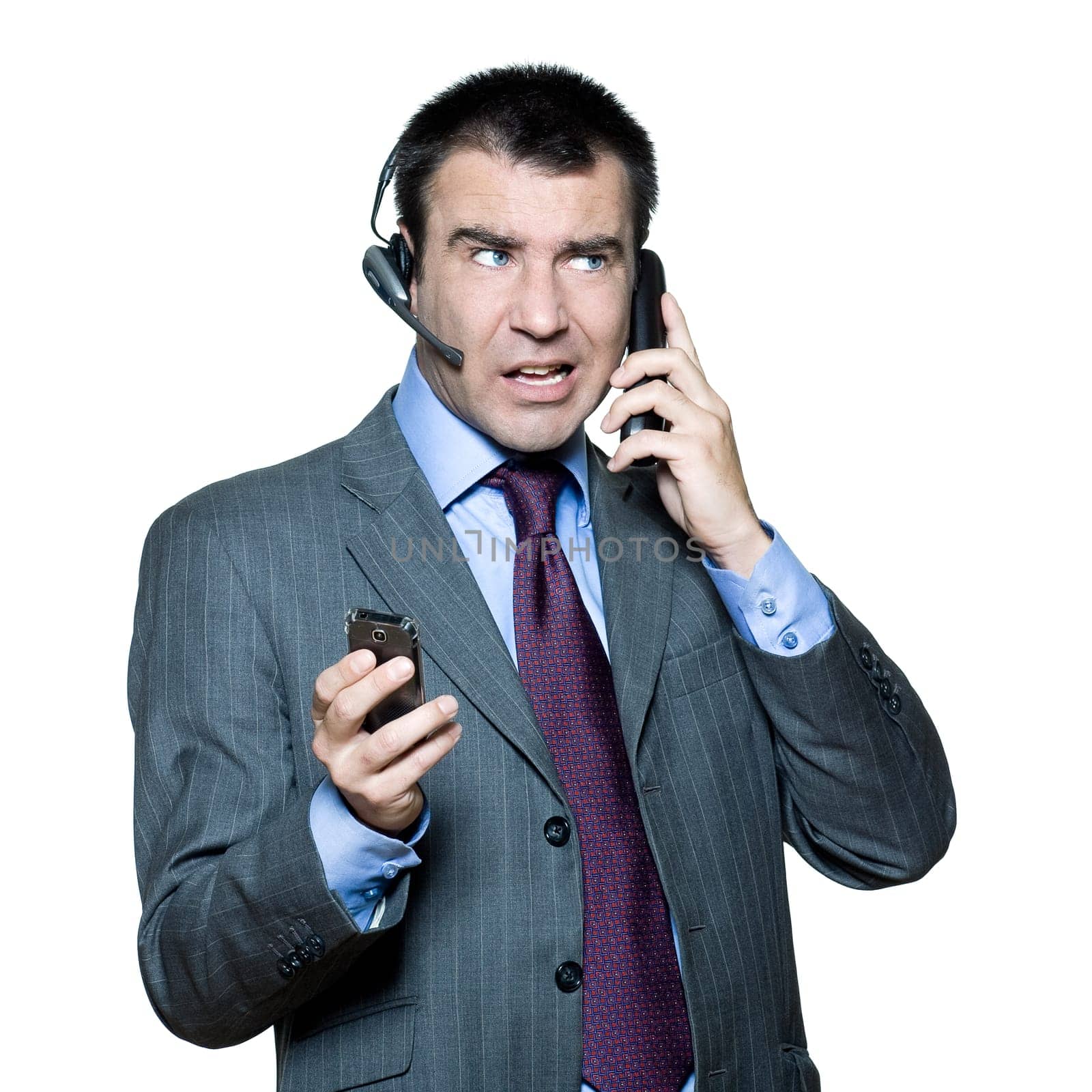 Portrait of businessman wearing headset and using mobile phone busy with multiple telephone in studio isolated white background