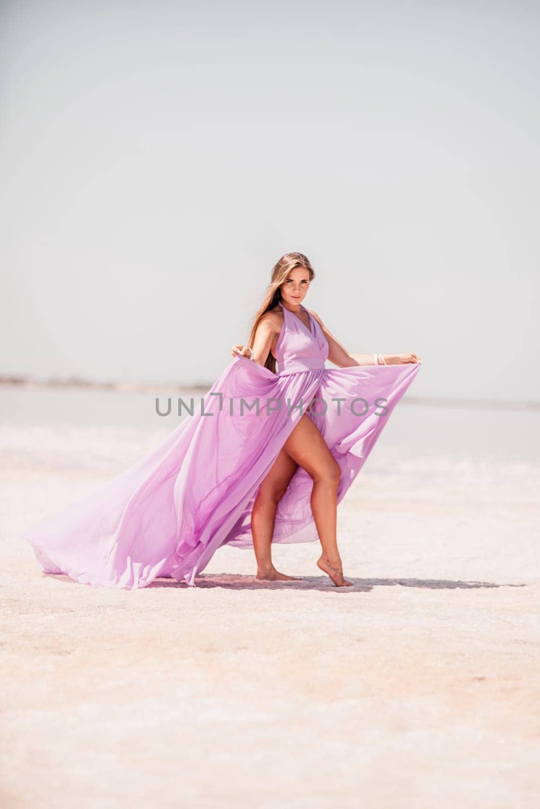 Woman pink salt lake. Against the backdrop of a pink salt lake, a woman in a long pink dress takes a leisurely stroll along the white, salty shore, capturing a wanderlust moment