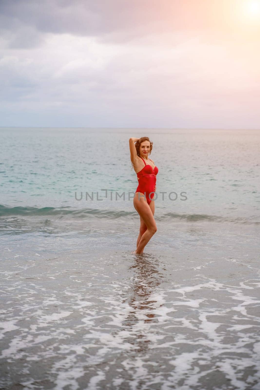 A beautiful and sexy brunette in a red swimsuit on a pebble beach, Running along the shore in the foam of the waves.