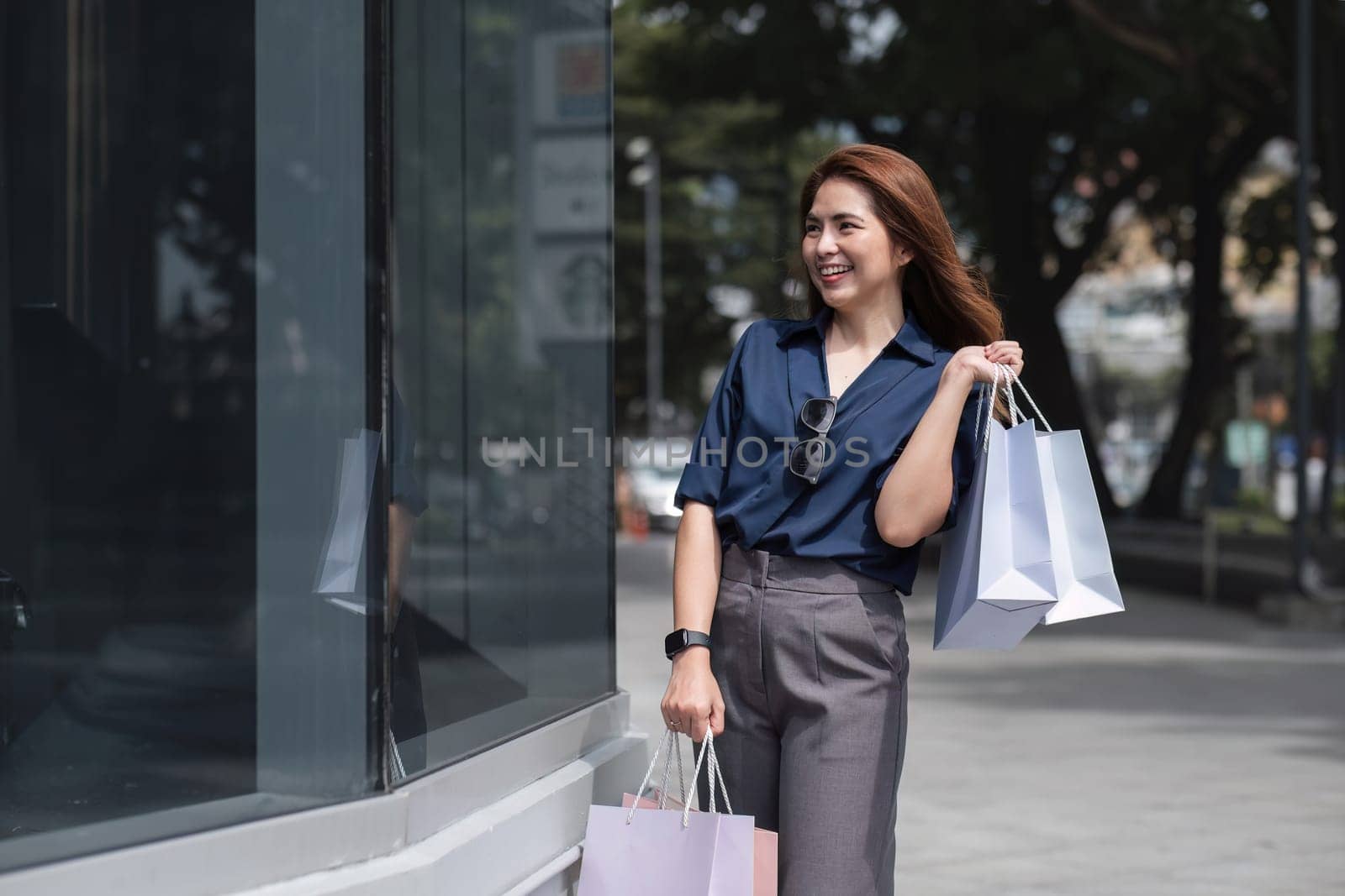 Happy tourist woman asian with shopping bags walks through the sunny street. Beautiful woman enjoys the weather after shopping. Consumerism, shopping. Active lifestyle.