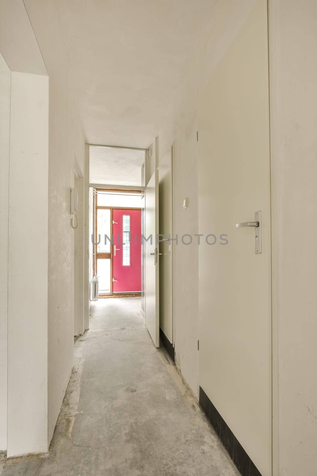 an empty room with red door and white walls in the middle of the room, there is no people or objects to be seen