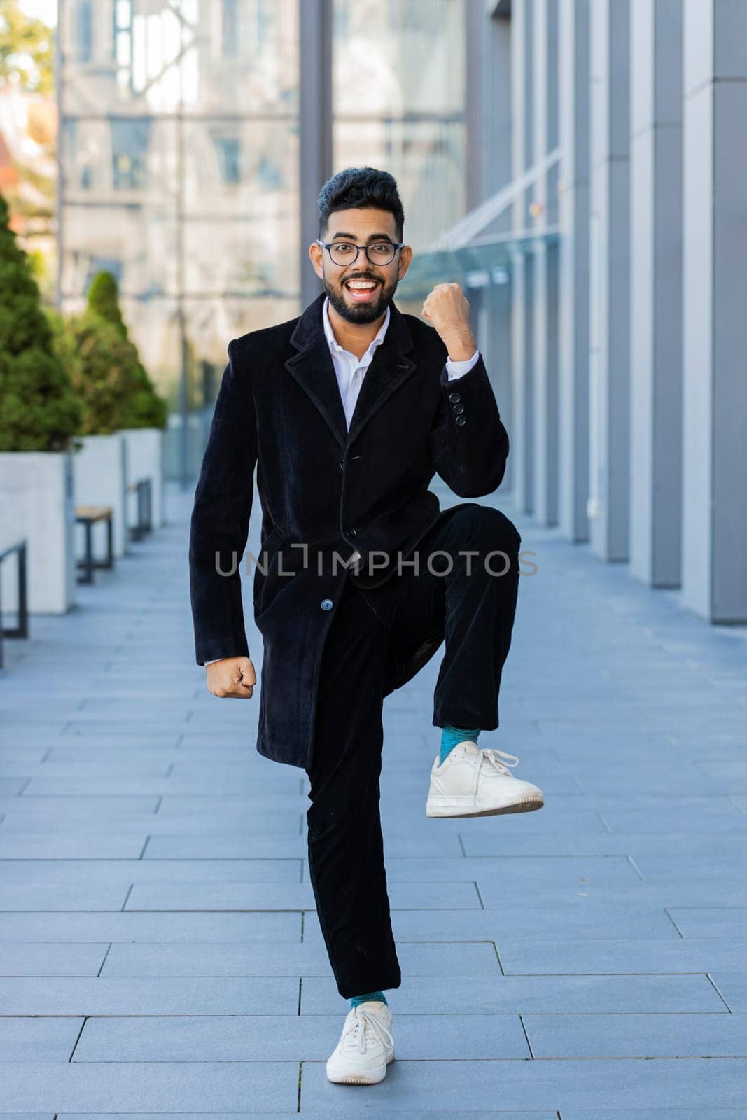 Happy Indian business man celebrating success, winning, career achievement, good news luck, victory, successful signing of contract. Arabian Hindu freelancer in downtown city street outdoors. Vertical