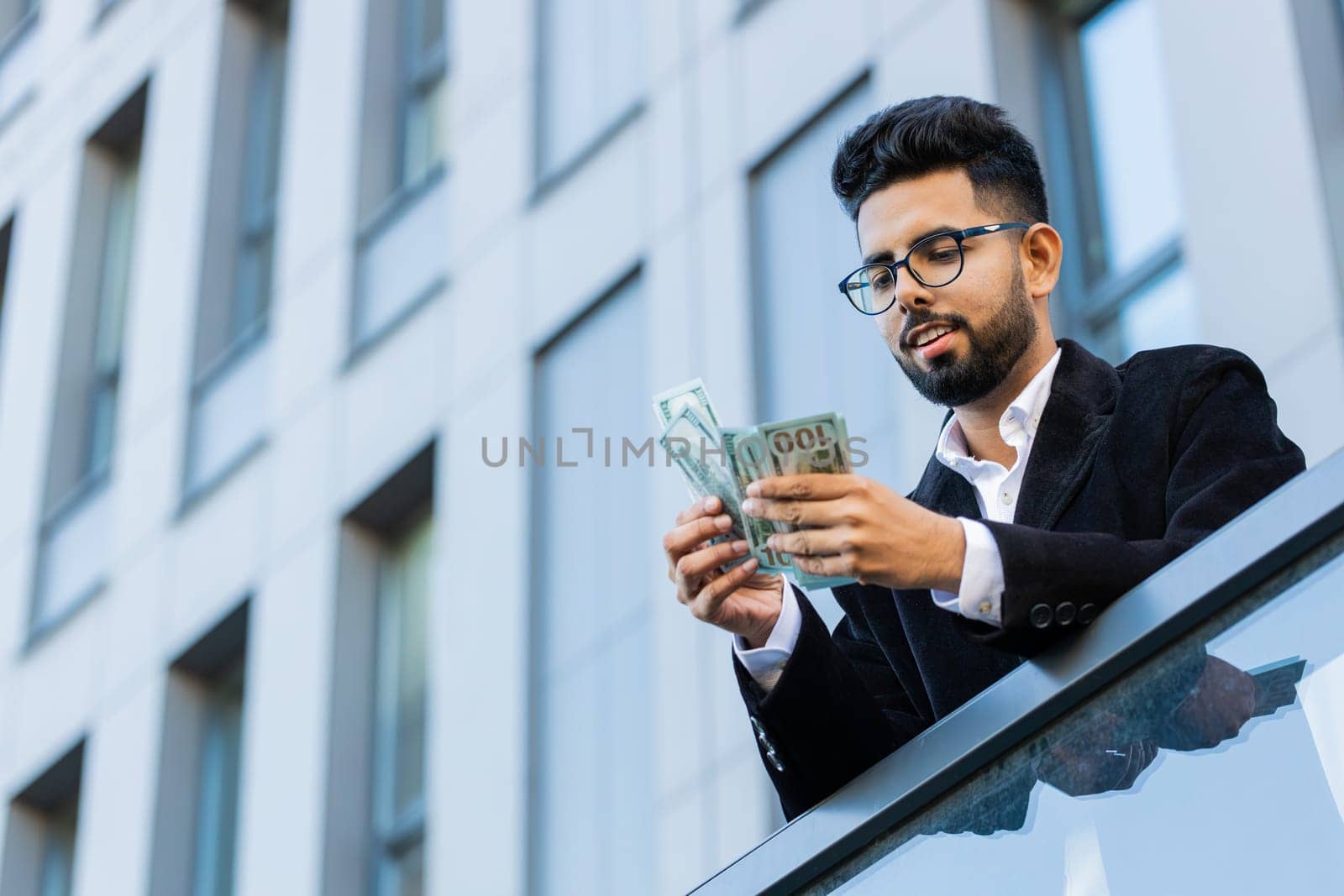 Happy rich Indian businessman winner counting money cash dollars banknotes salary celebrate victory, profit finance income reward outdoors. Arabian Hindu freelancer in downtown city. Business people