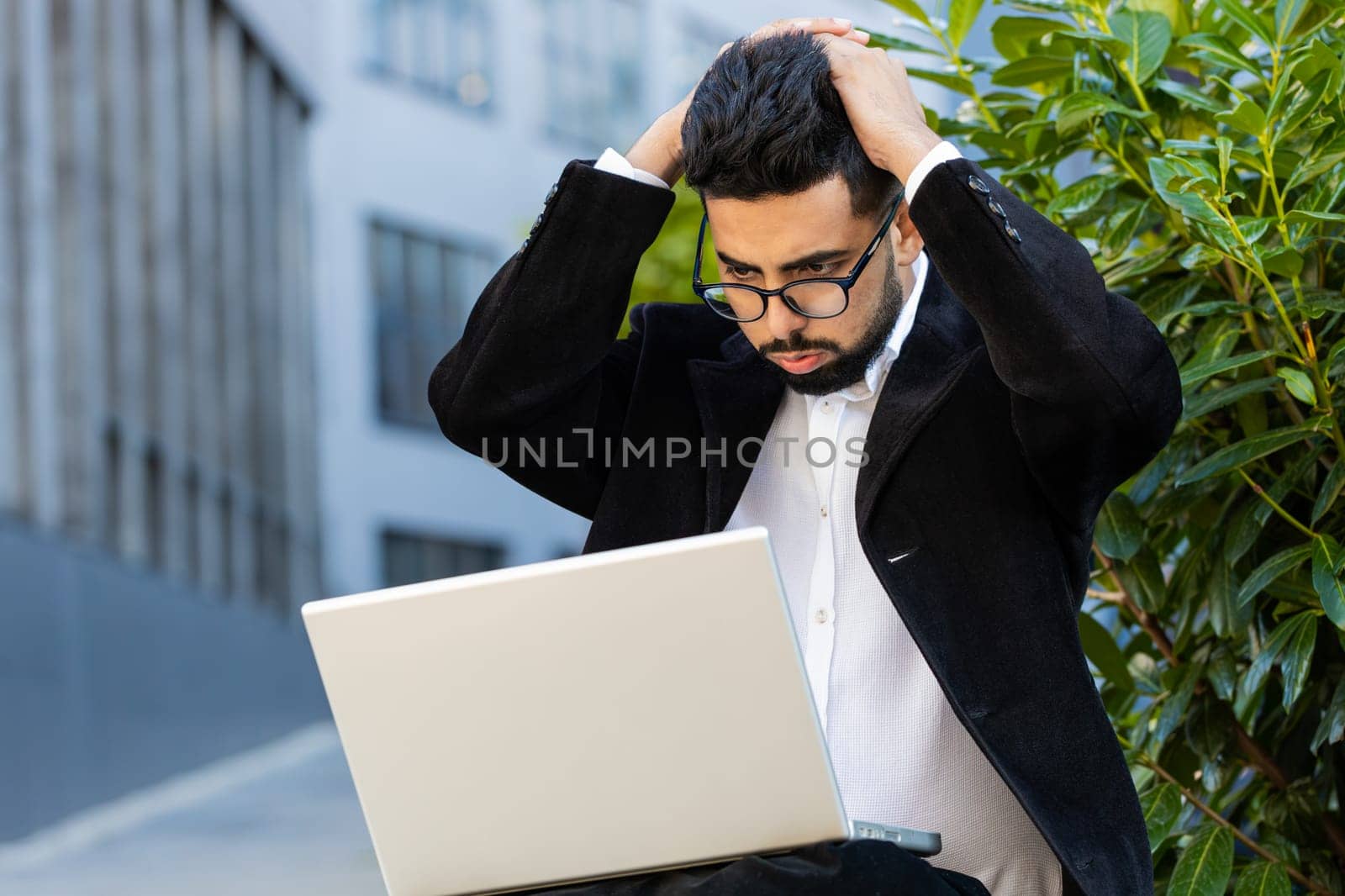 Displeased worried Indian businessman use laptop notebook typing browsing working loses bad news loss database fail computer virus error problem outdoor. Arabian Hindu freelancer executive manager ceo