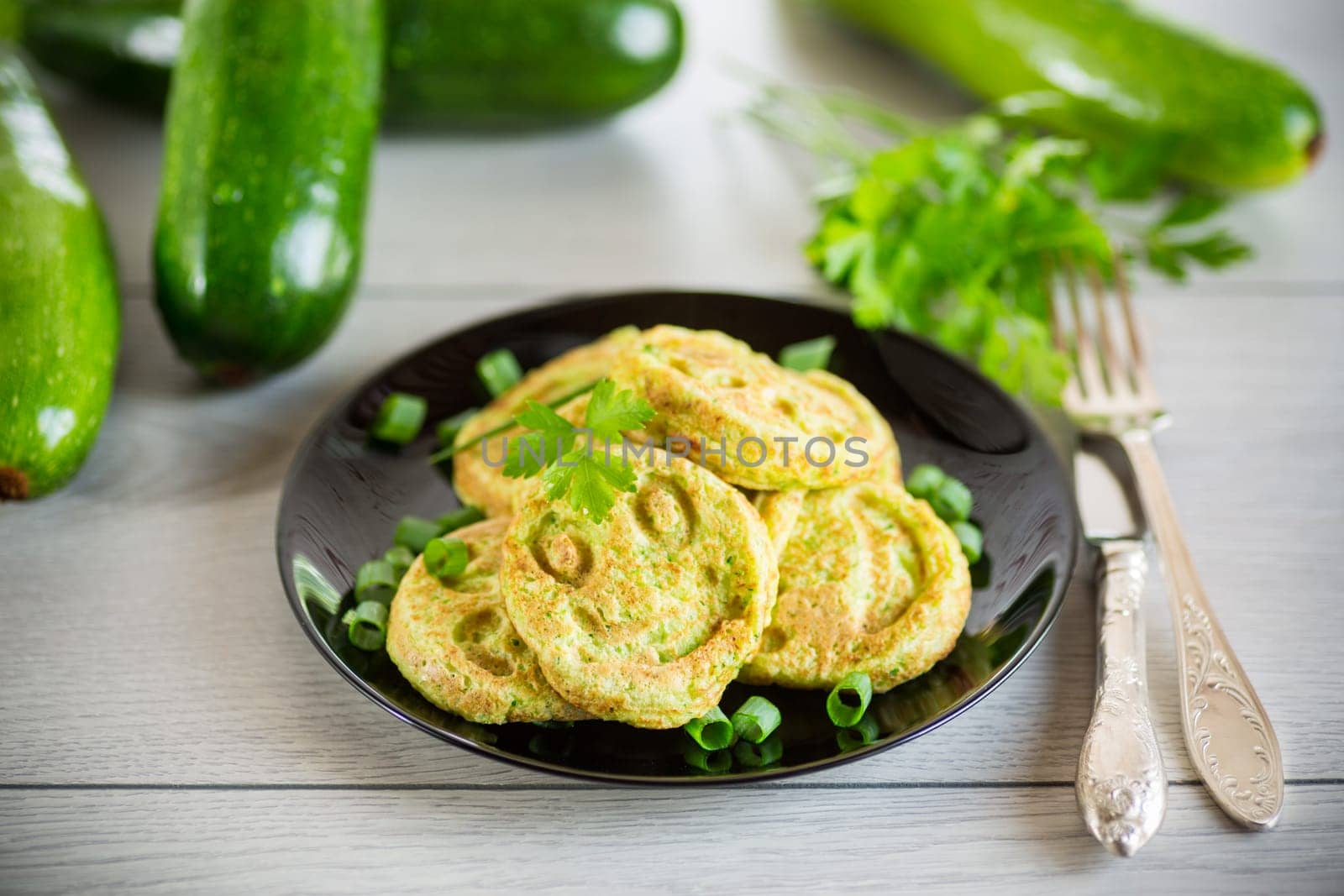Fried squash green pancakes in a plate, on a wooden table.