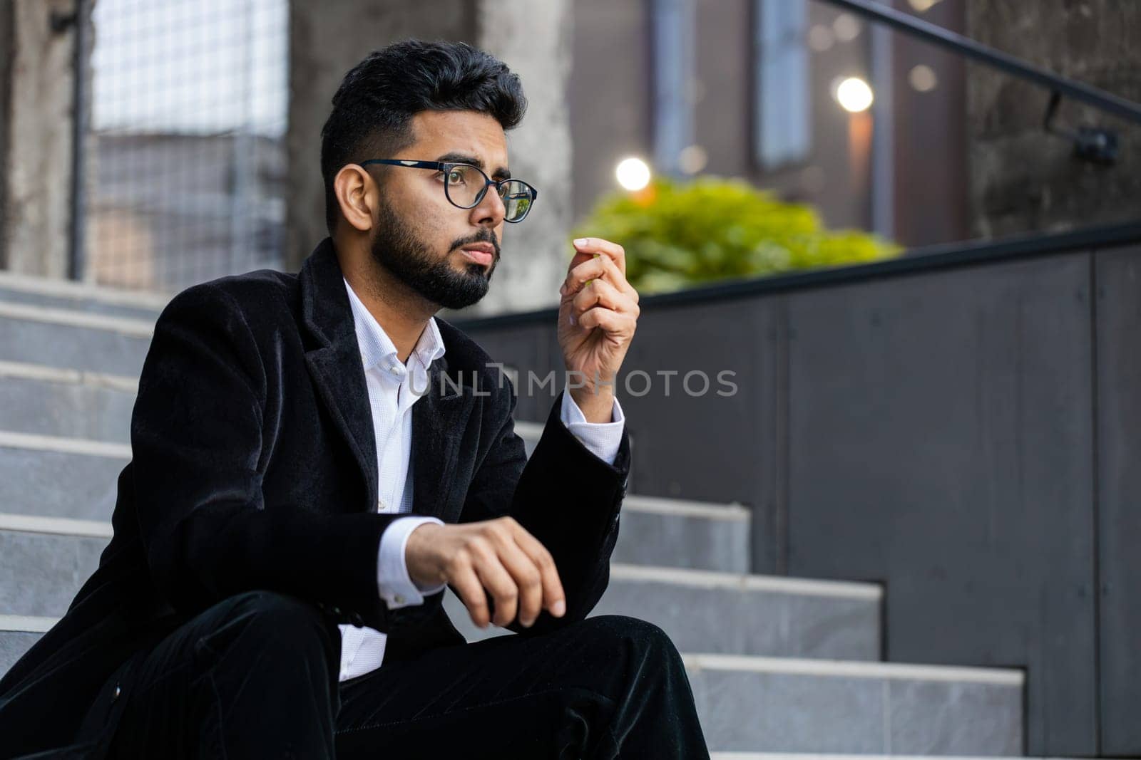 Unhappy sad Indian business man frustrated stress pensive feeling bad after company unemployment lost job problem solution crisis outdoor. Arabian Hindu freelancer guy sitting on stairs downtown city