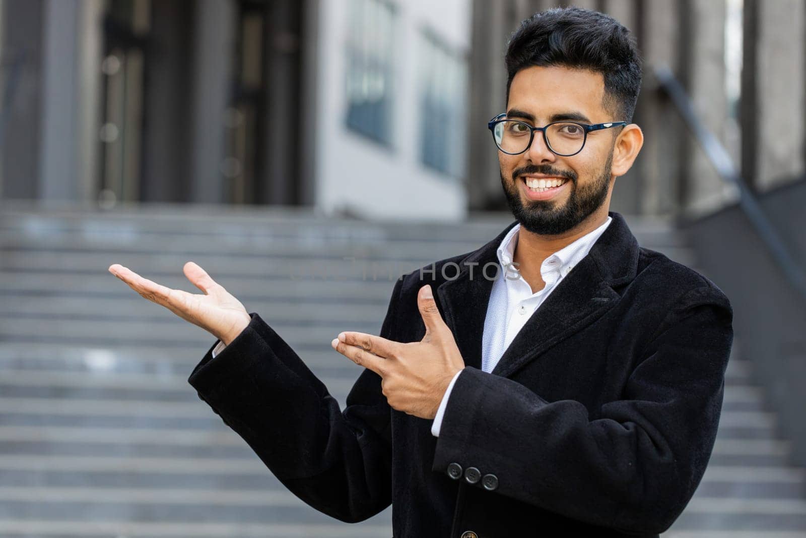 Indian businessman showing pointing empty place advertising area for commercial text copy-space for goods promotion outdoors. Arabian Hindu freelancer guy in downtown city street. Business people