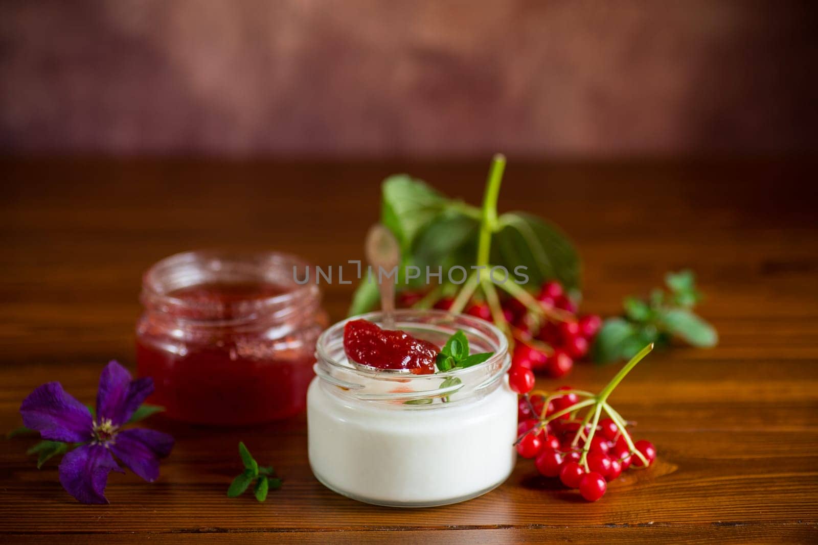 Prepared homemade yogurt with viburnum jam and viburnum on a wooden table.