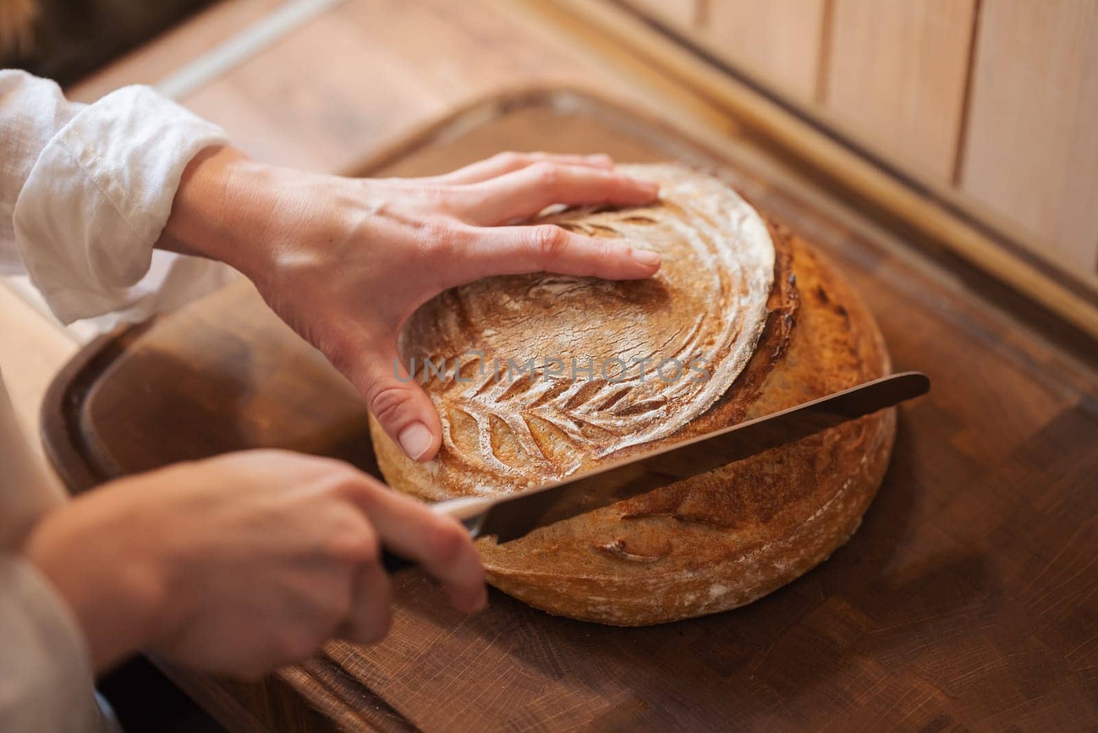 Female hands with a knife, starting to cut the fresh loaf of bread, close up