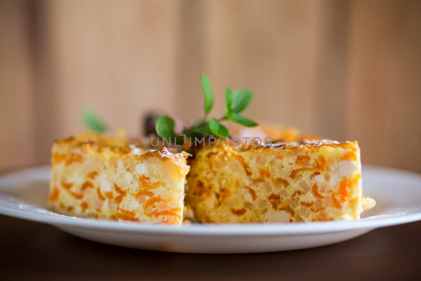 Cooked cottage cheese casserole with pieces of pumpkin inside, on a wooden table.