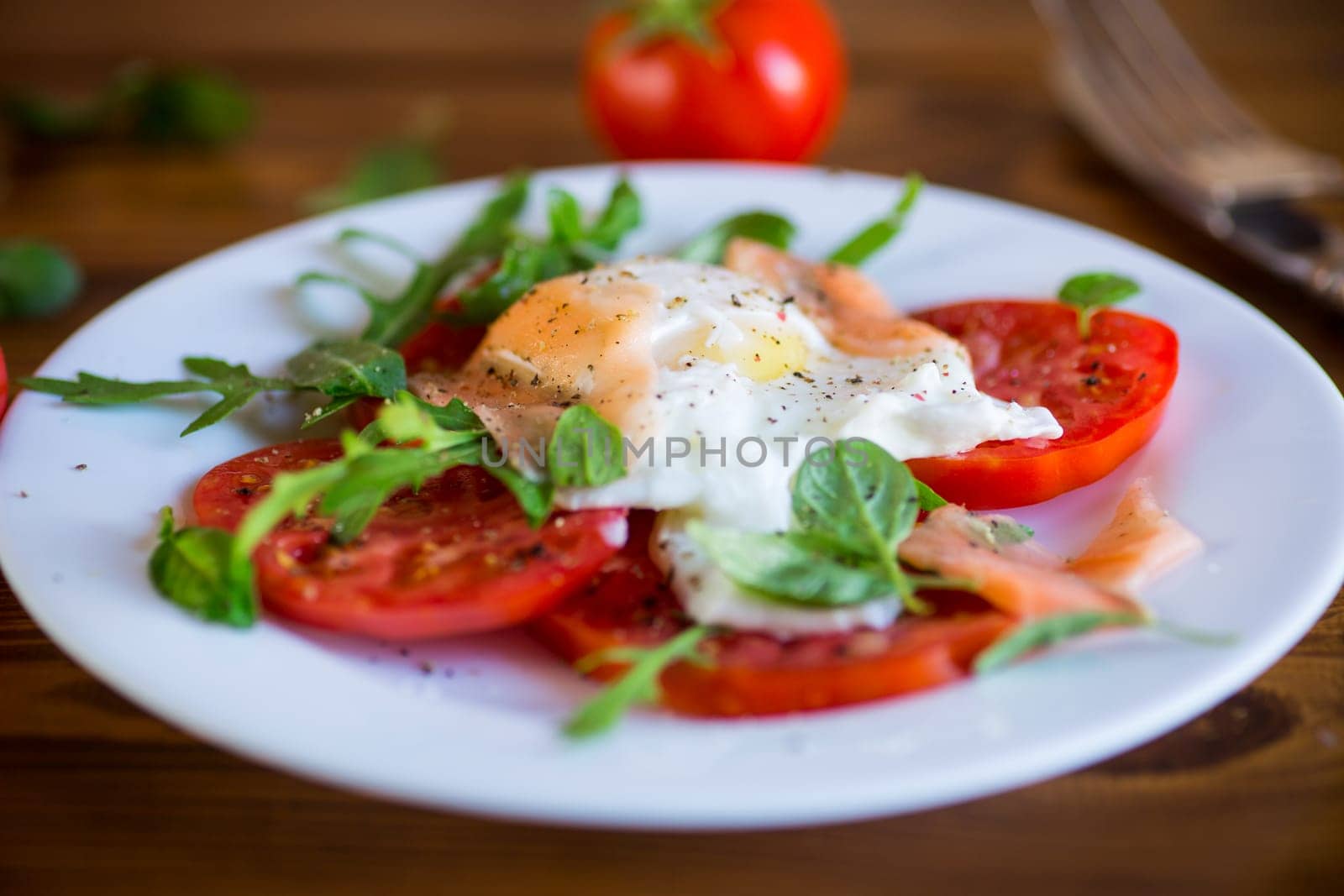 Cooked poached egg with herbs, lightly salted salmon and tomatoes with spices on a wooden table.