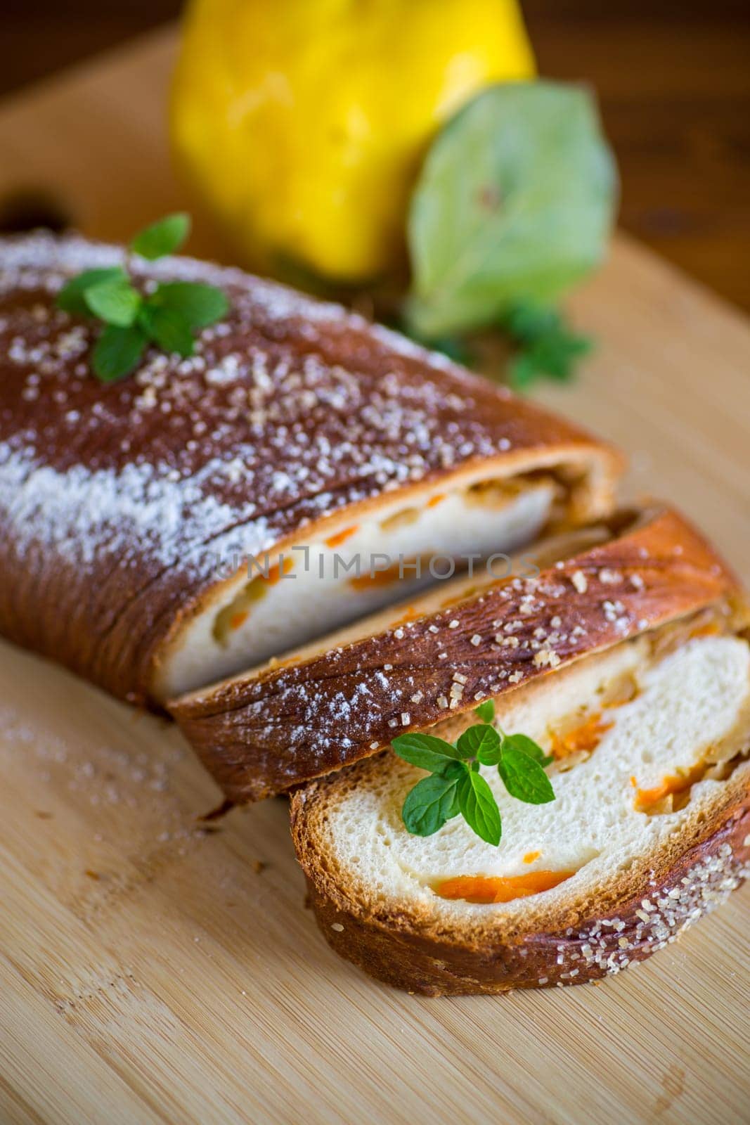 Cooked sweet pie with quince and pumpkin inside, yeast dough roll, on a wooden table.