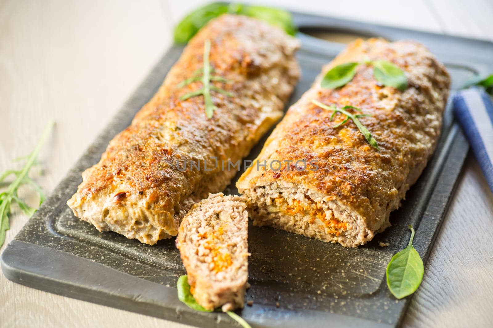 Cooked minced meatloaf with vegetable filling inside, on a wooden table.