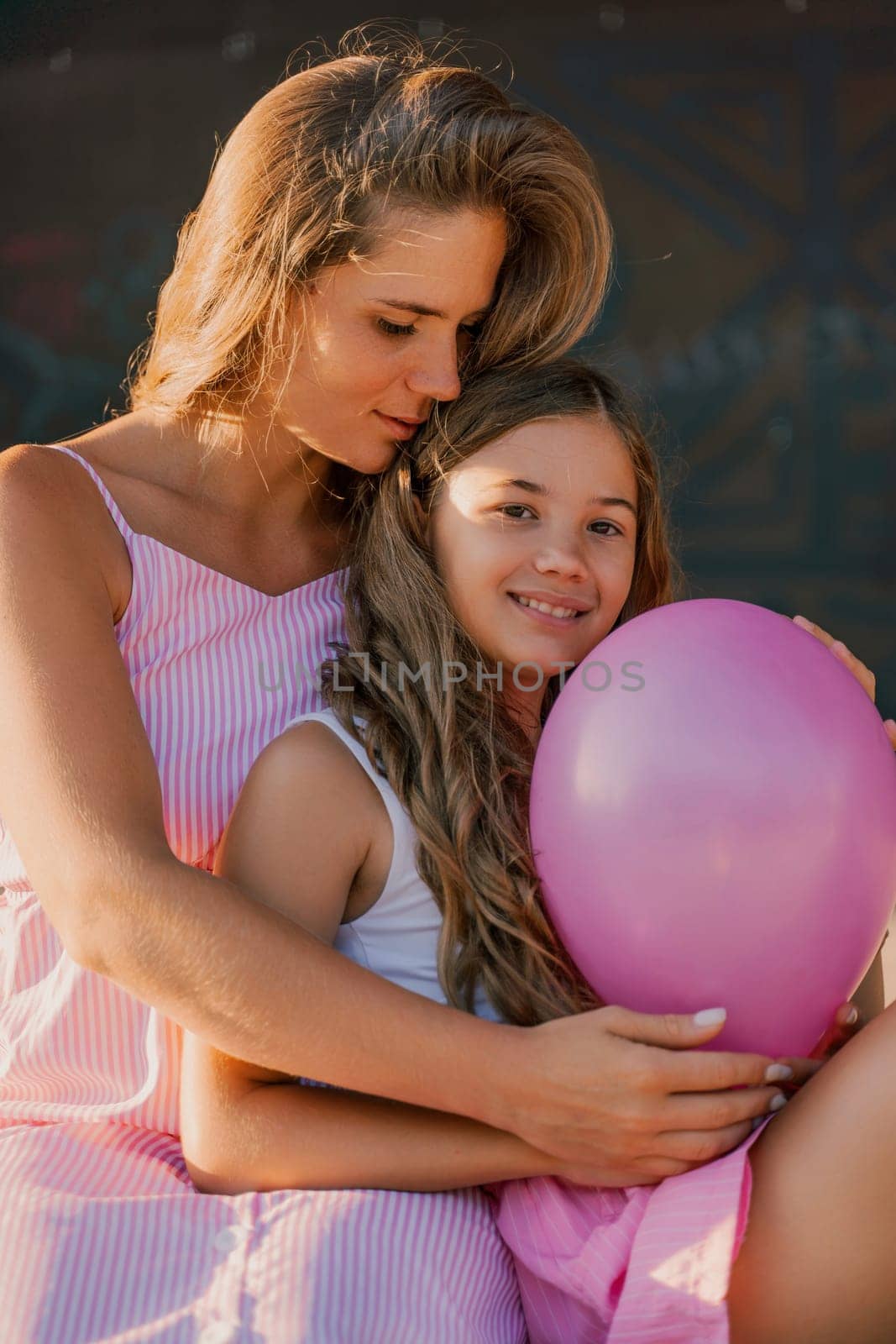 Portrait of mother and daughter in pink dresses with flowing long hair against the black backdrop. The woman hugs and presses the girl to her. by Matiunina