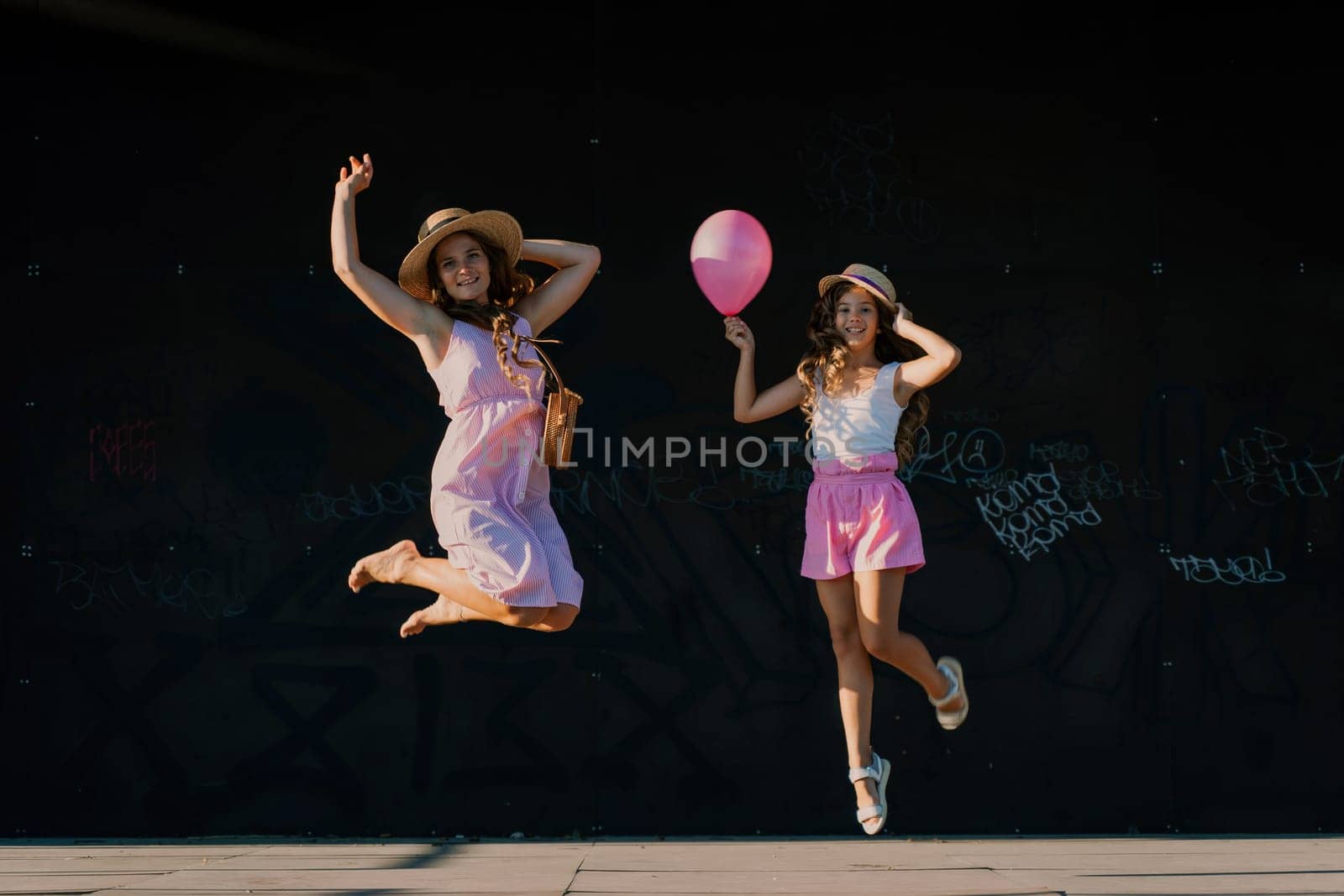 mother and daughter jumping in pink dresses with loose long hair on a black background. Enjoy communicating with each other.