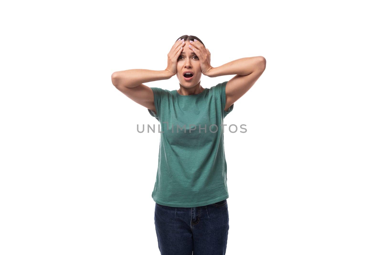 young excited black-haired woman with collected hair is dressed in a basic t-shirt and jeans holding her head.