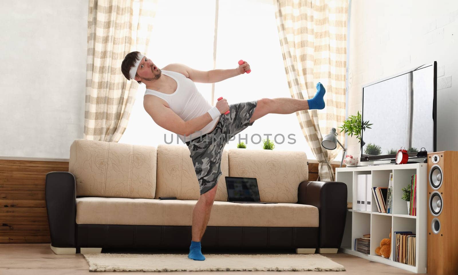 Young handsome man in shorts and vest holds pink dumbbells in hand. Watch tv lessons single combats is practicing receptions of sensei one home fitness indoor training independent education remotely