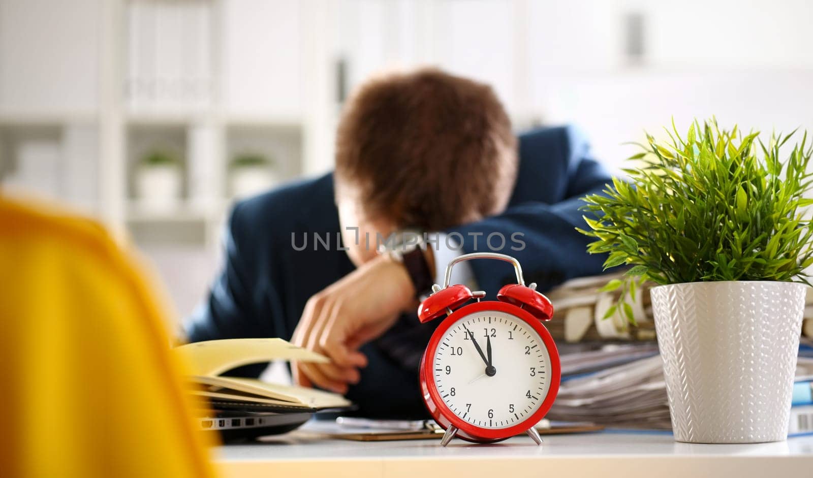 Red alarm clock shows late time closeup and tired office male clerk in suit take nap on table workplace full of exam papers. Career frustration freelance employment fail study problem low energy down