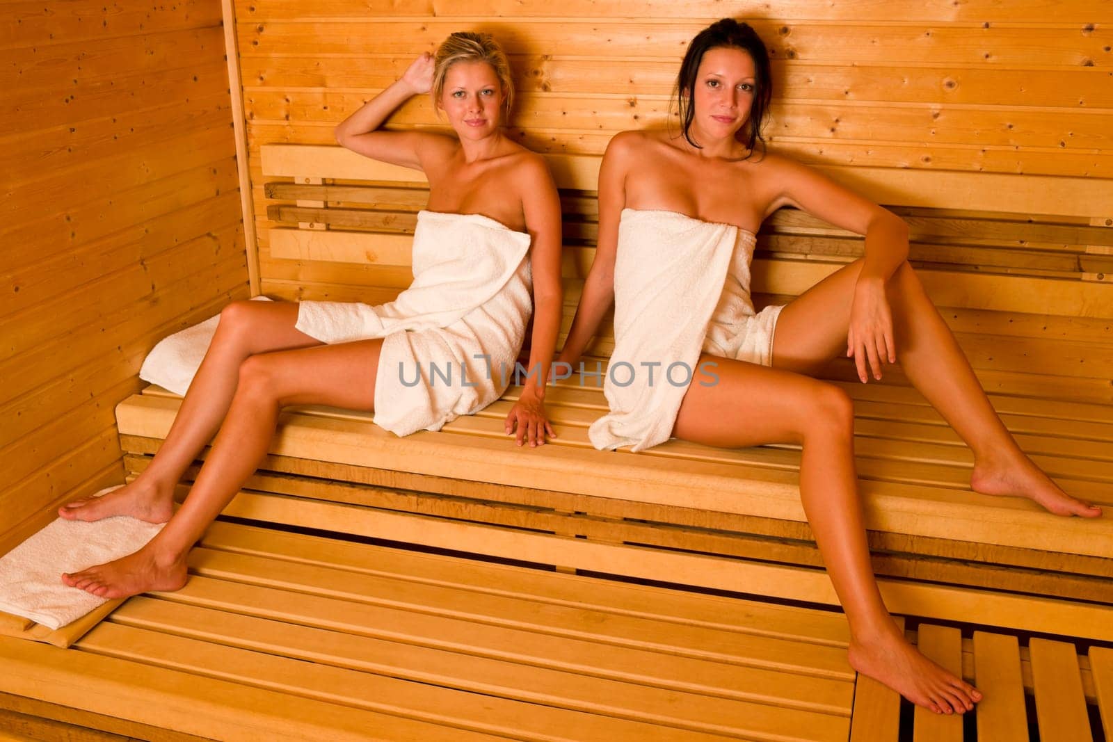Sauna two healthy beautiful women relaxing sitting wrapped in towel