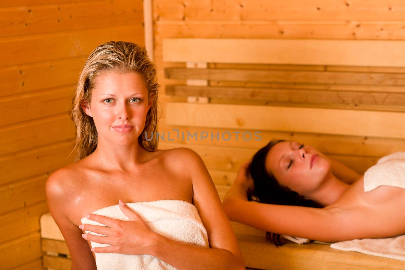 Sauna two healthy beautiful women relaxing sweating lying covered towels