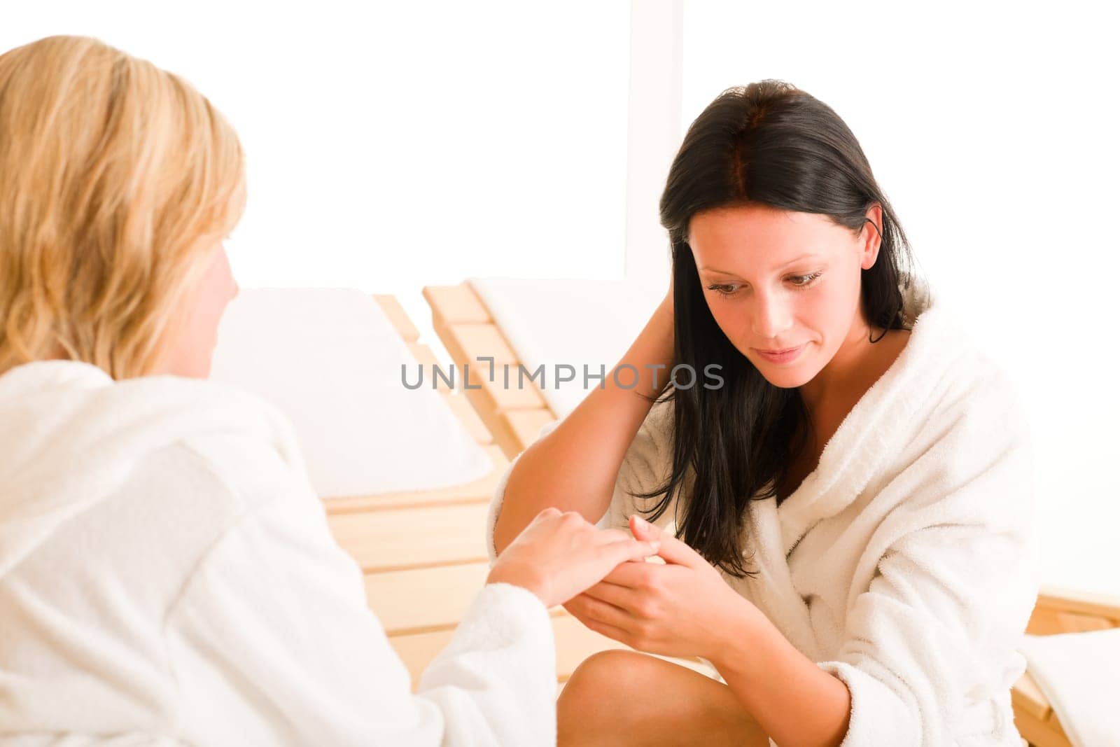 Beauty luxury spa room two women relax sun-beds show manicure