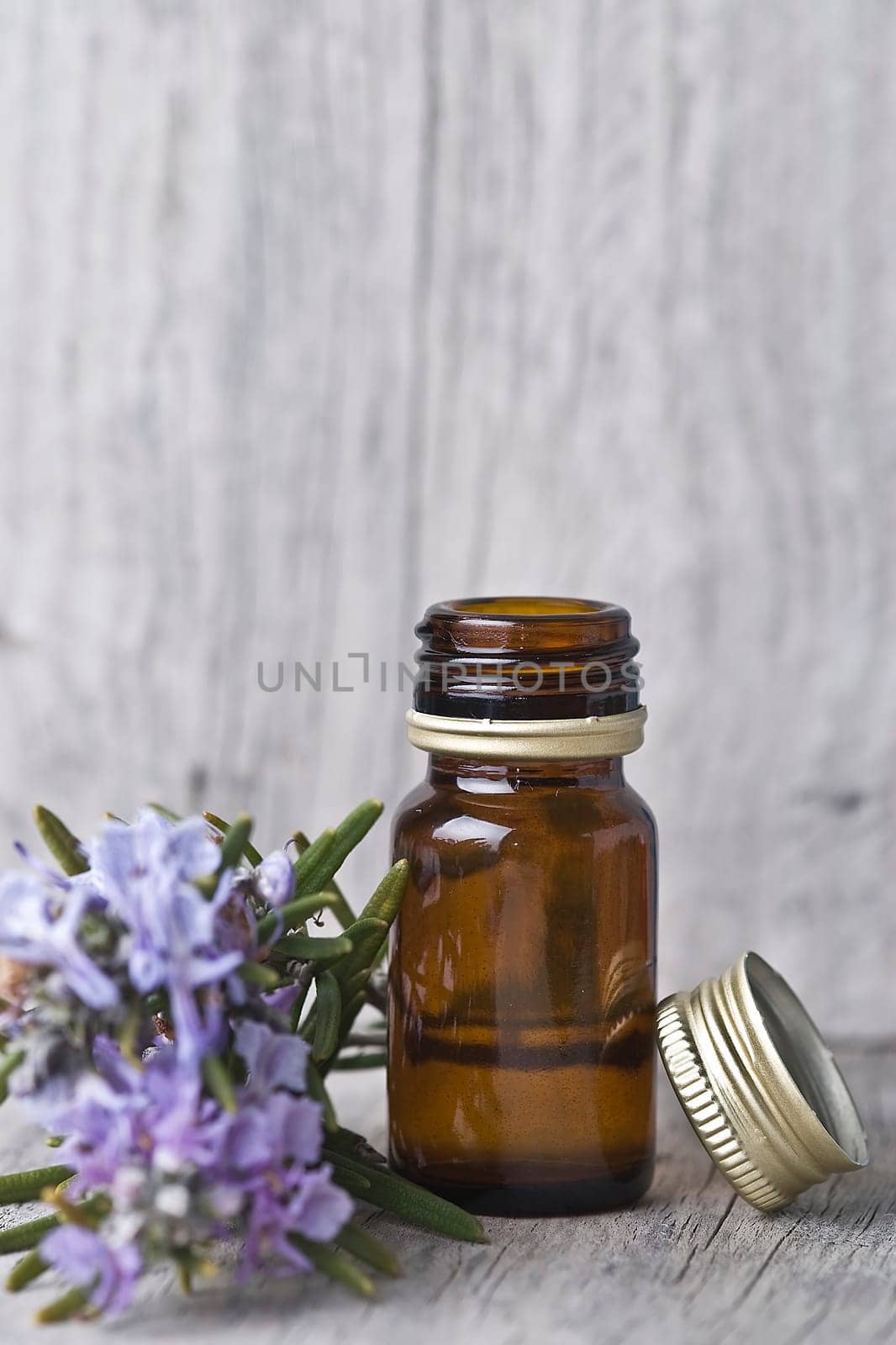 Rosemary branches and a bottle of rosemary essence on an old wooden shelf.