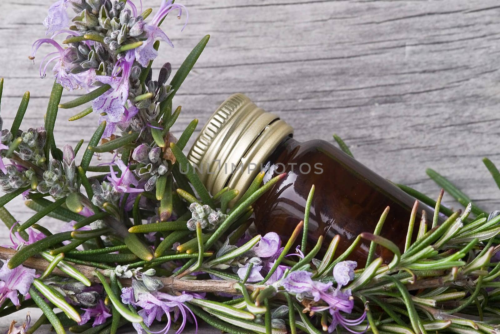 Rosemary branches and a bottle of rosemary essence on an old wooden shelf.