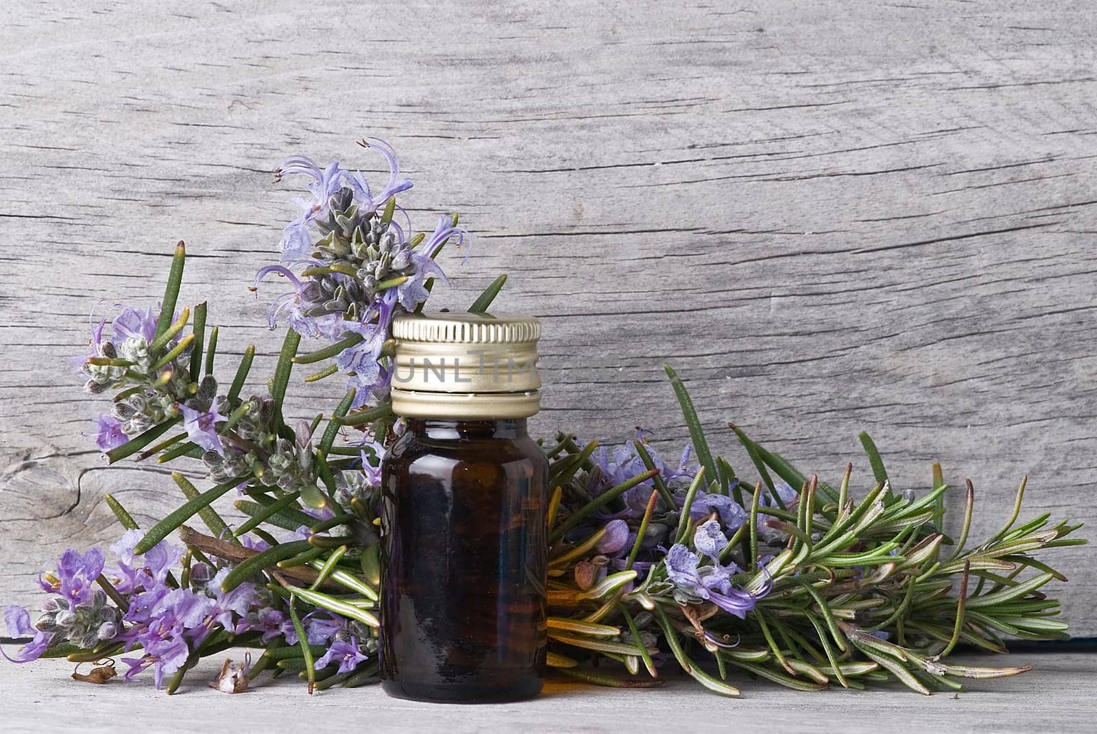 Rosemary branches and a bottle of rosemary essence on an old wooden shelf.