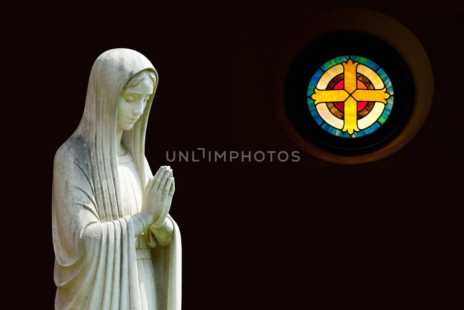 Statue of Mary praying in profile with isolation path and out of focus cross shaped window on the right
