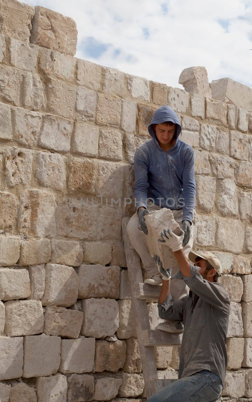 Goreme, Turkey - June 2011: Two Turkish builders up ladders on construction site passing random size stone blocks building dwelling