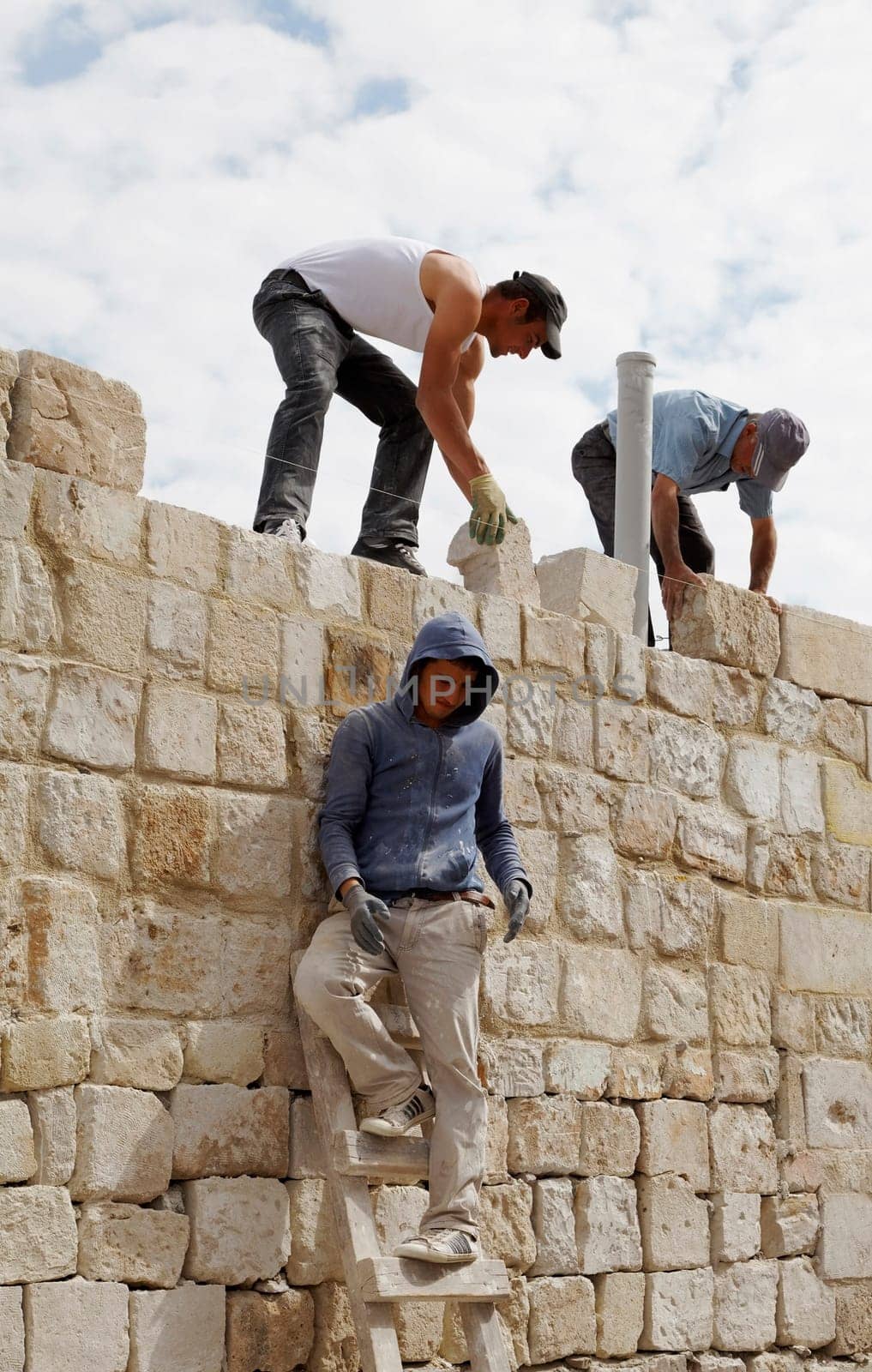 Goreme, Turkey - June 2011: Turkish builders on construction site building dwelling with random size limestone bricks, portrait, crop space and copy area