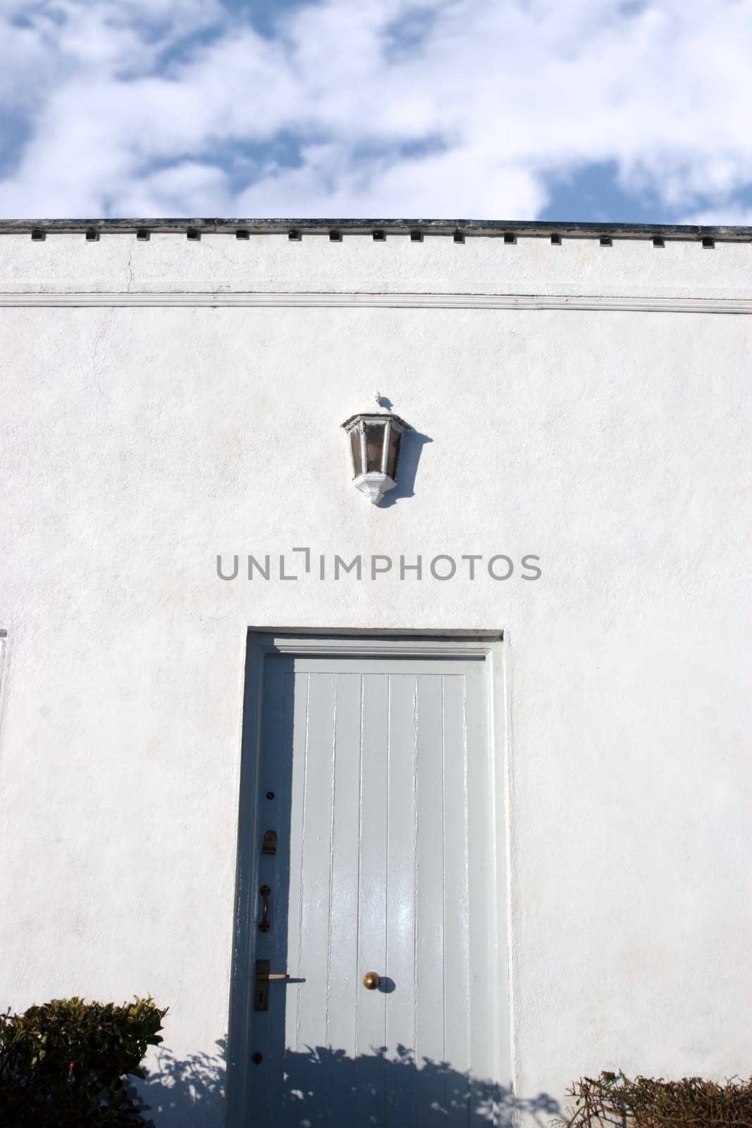 a blue grey front door on white wall with sky above