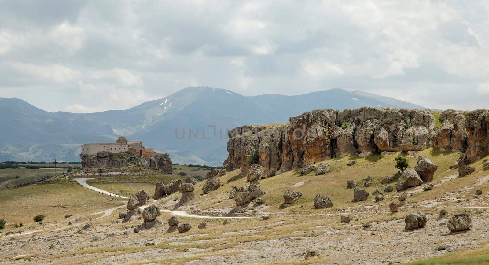 volcanic lava ash terrain with old church on a hill and mountain range in background Cappadocia , dirt tracks, cloudscape, landscape crop space and crop area