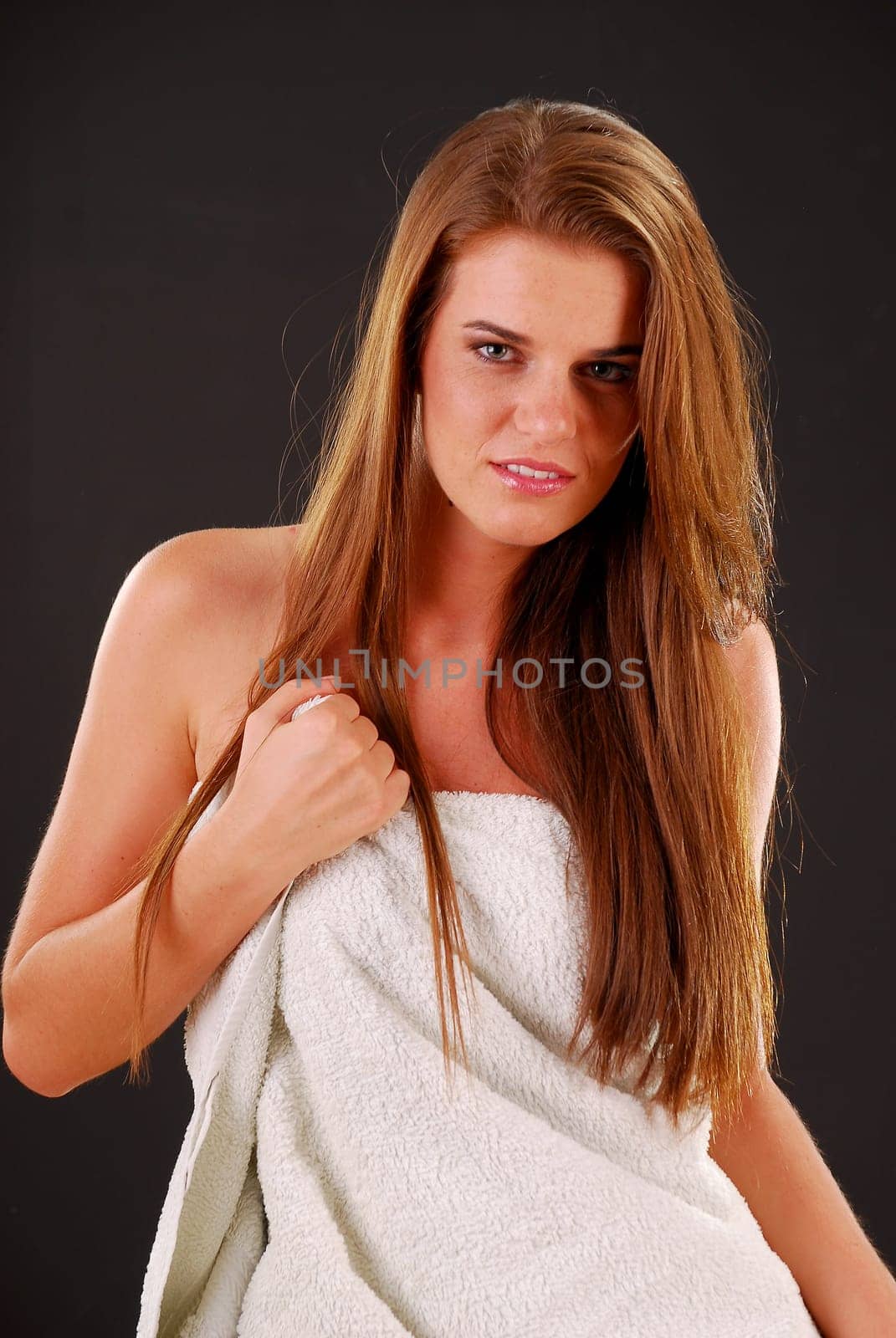Portrait of young woman with a towel sitting on bed on dark background