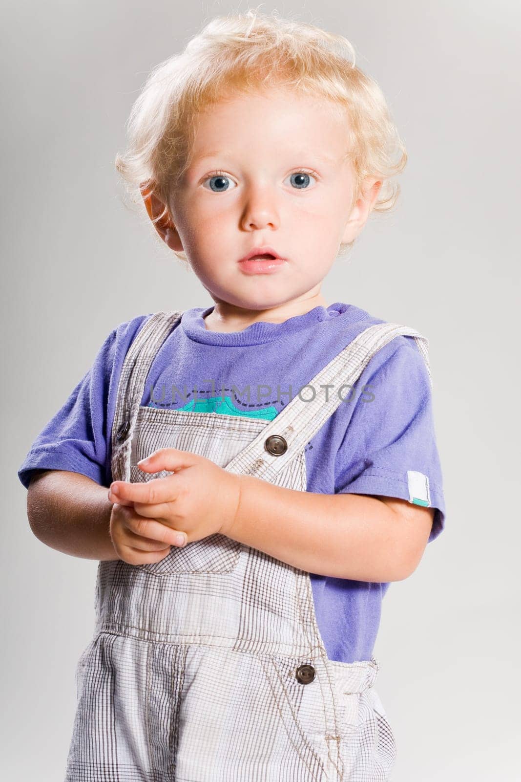 Blond boy in dungarees against white background