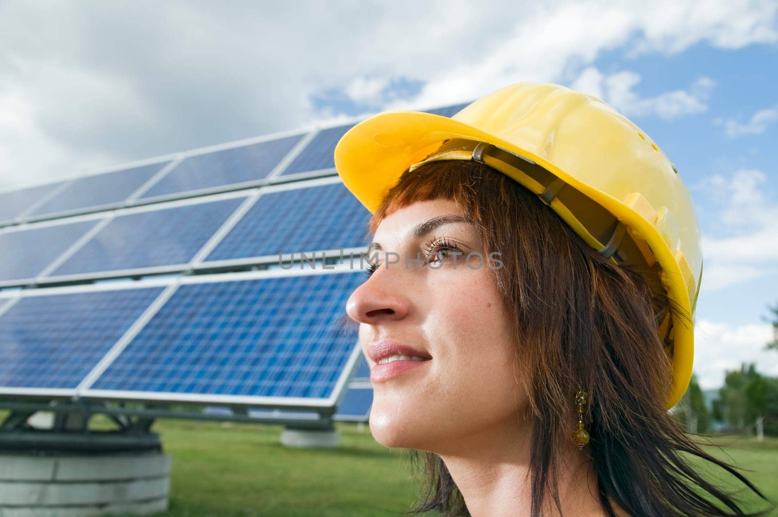 Side head portrait of a young brunette woman with yellow construction helmet as a headgear and optimistic view to the side
