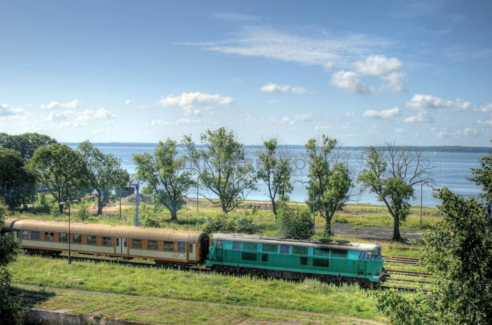 Passenger train leaving the station against the lake and blue sky