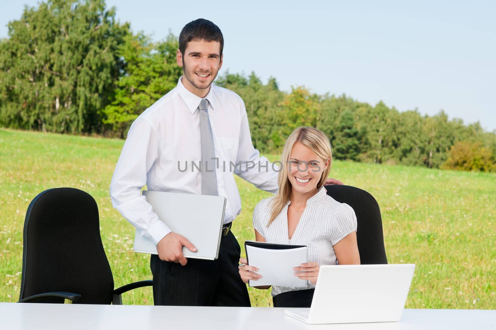 Young business colleagues in nature office smile behind table