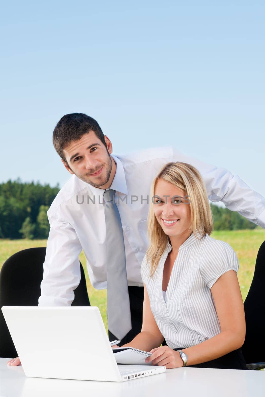 Young business colleagues in nature office smile behind table