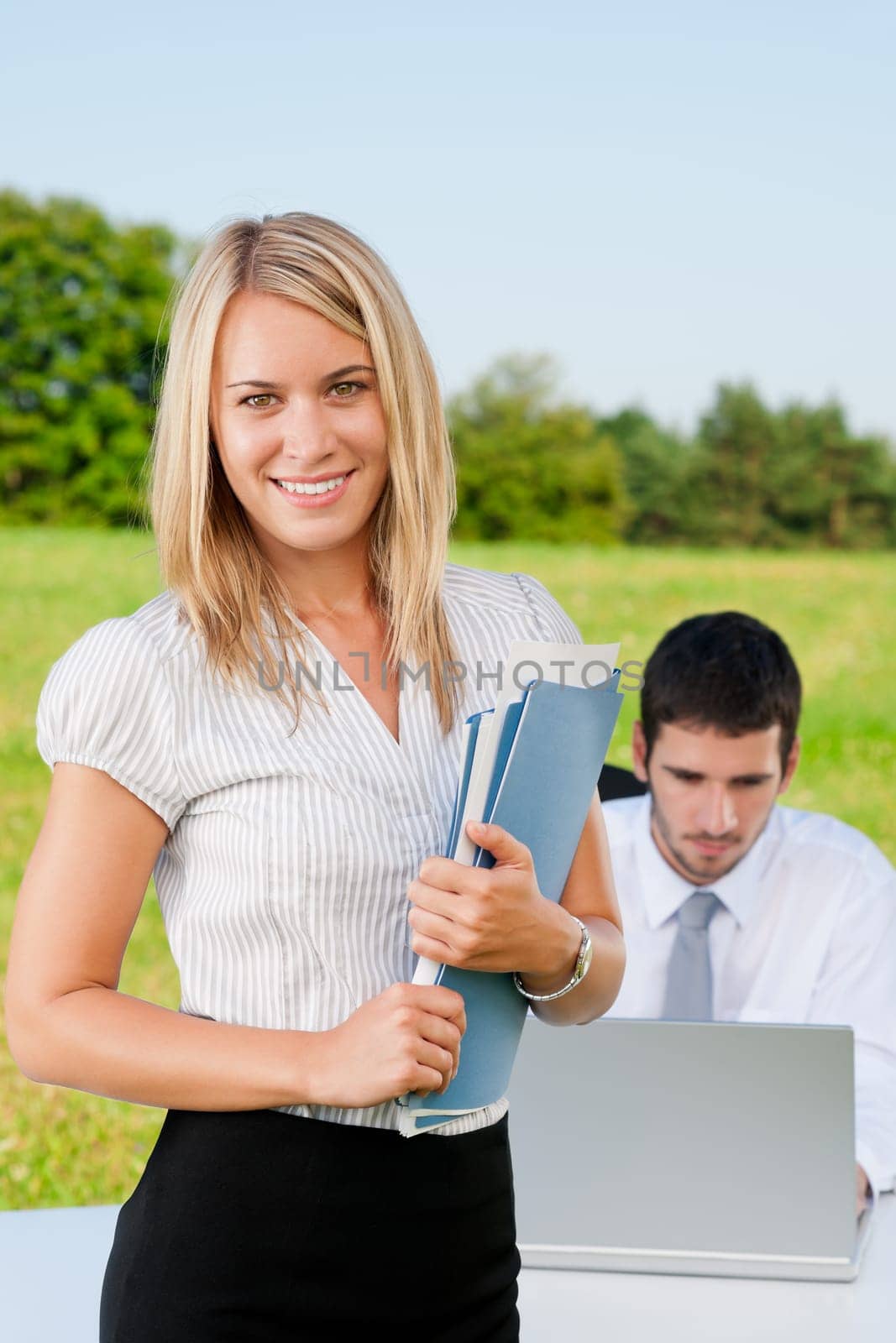 Young businesswoman in sunny nature with folders and male colleague
