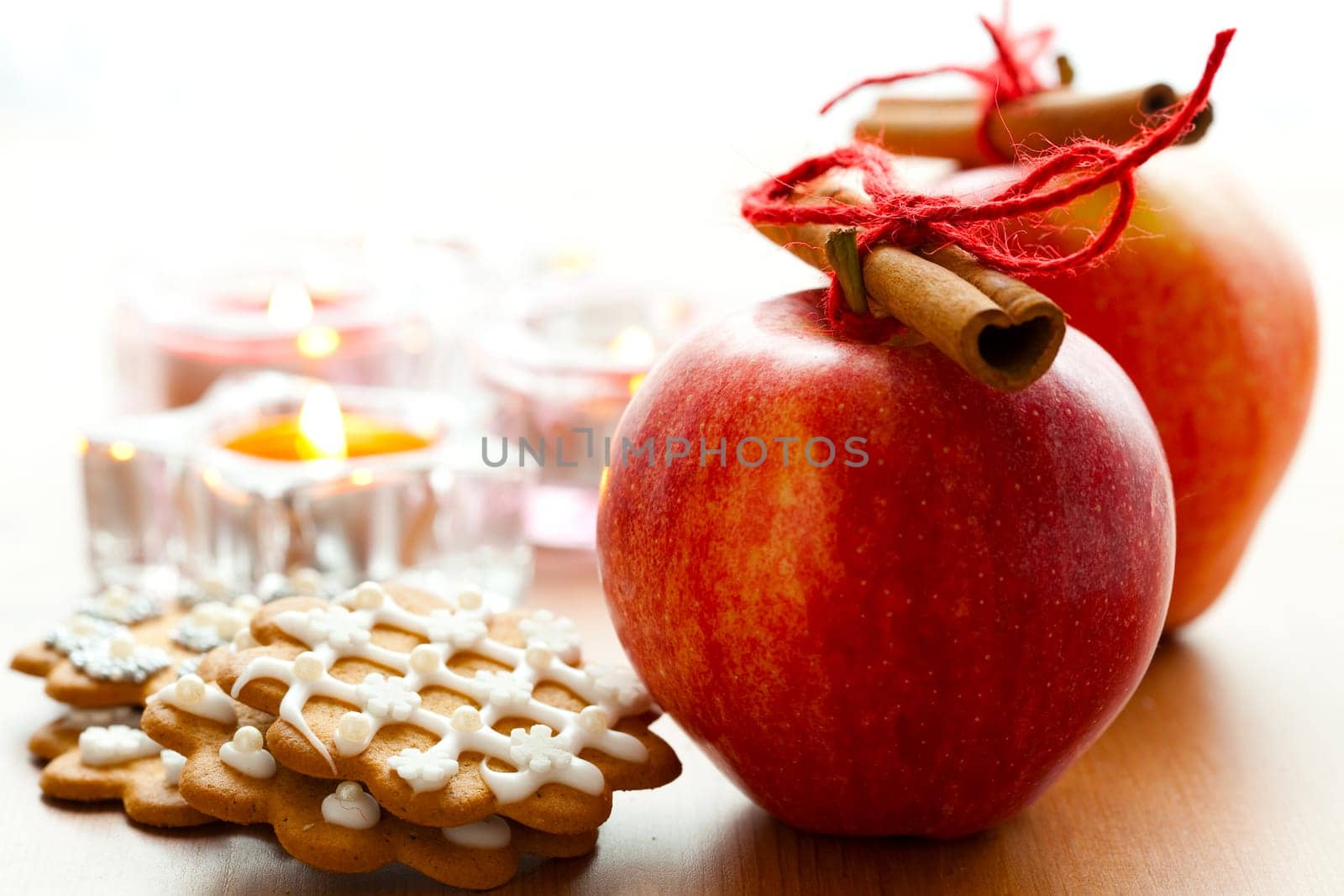 Close-up of delicious red Christmas apples with cinnamon sticks, gingerbread cookies and candles