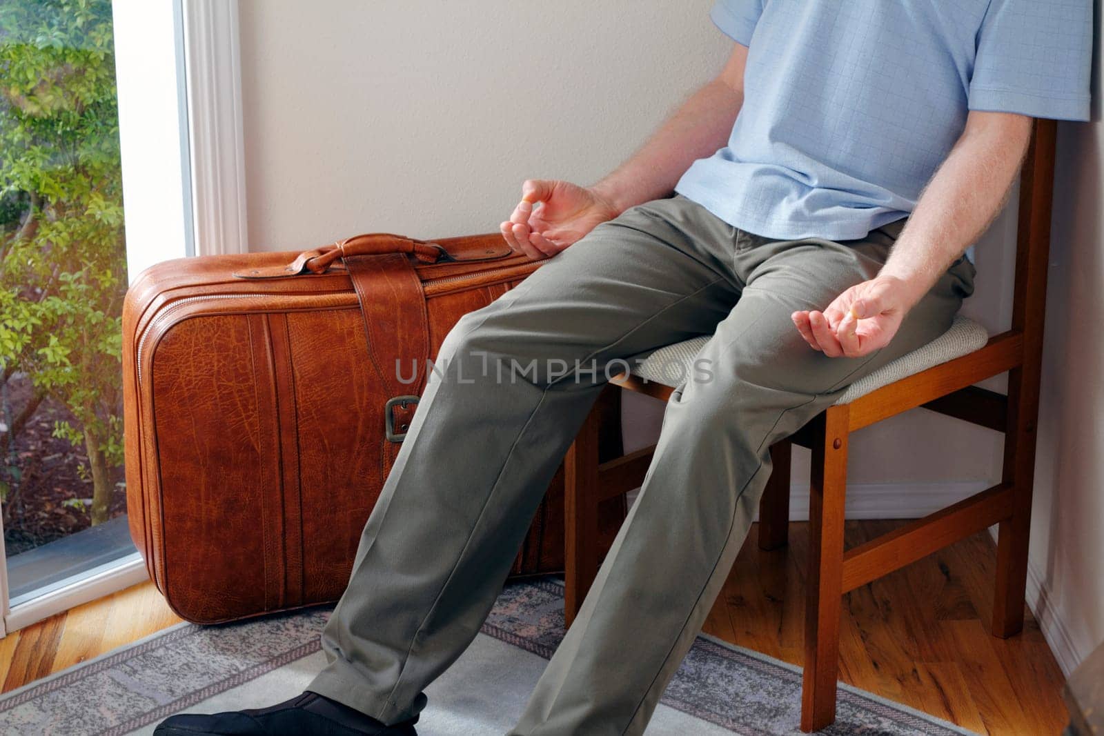 In a home foyer with a suitcase near door a male sits in a chair meditating before traveling to help have a peaceful journey.