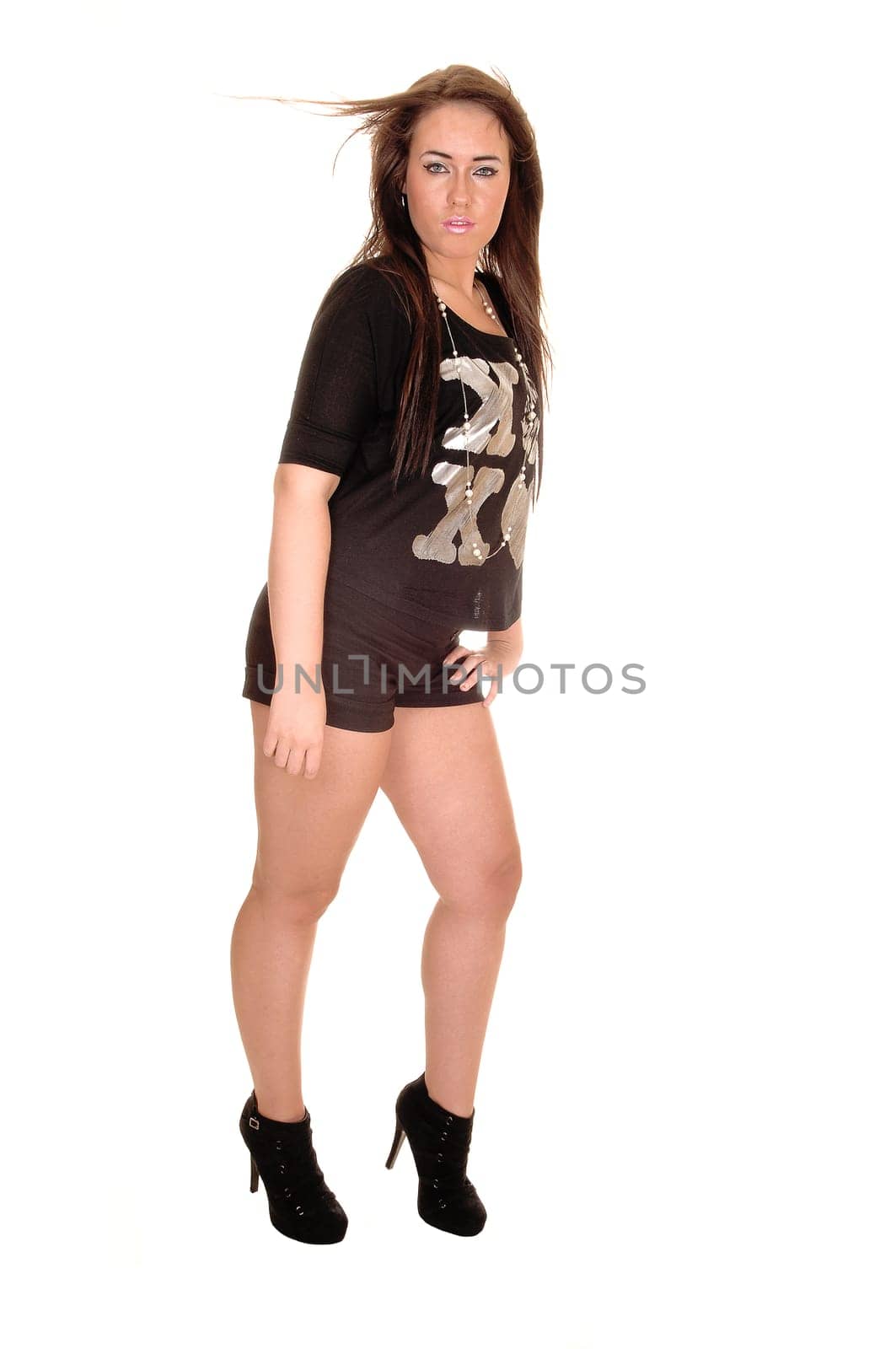 A pretty girl standing in the studio and the wind is blowing into  her hair, in black shorts and top, over white background.
