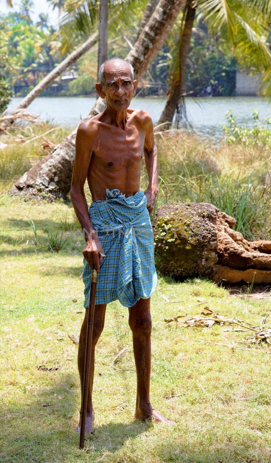 Kerala, India -  September 25, 2011: Indegenous old man with walk stick and traditional blue loin cloth, full length with crop margins