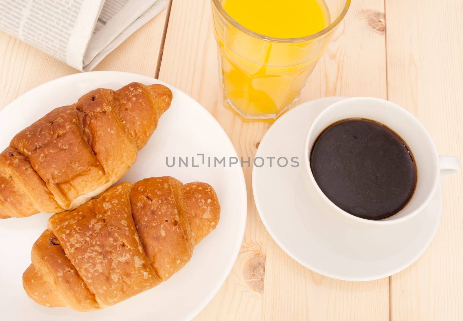 Breakfast - Croissants, Coffee, Orange Juice and Newspapers on Wooden Table