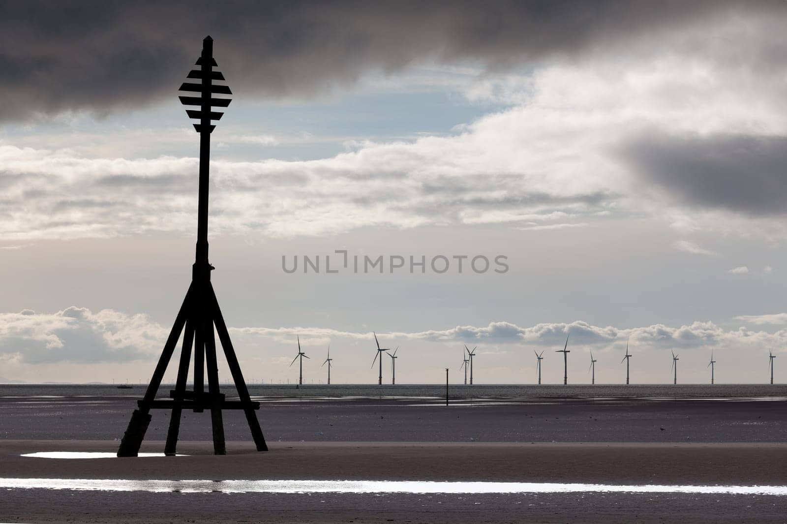 Wind turbines in the ocean off a sandy beach near Liverpool on a cold and cloudy day
