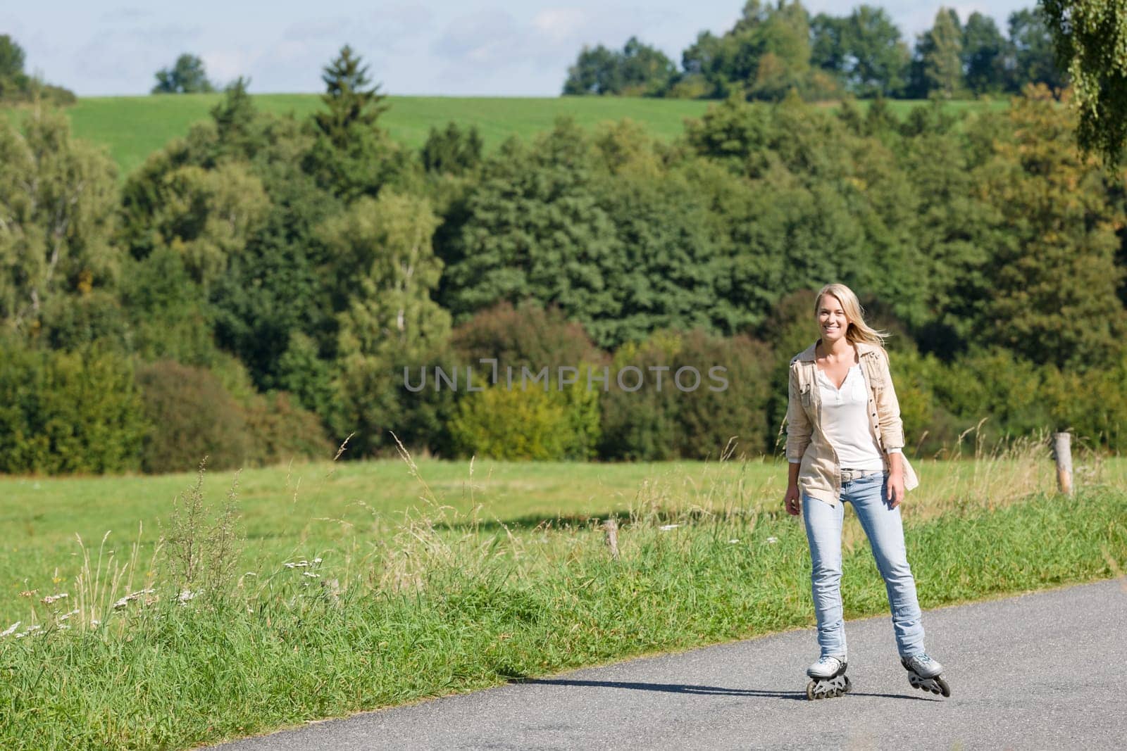 Inline skating young woman wearing jeans on sunny asphalt road